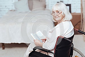 Positive retired woman reading book in wheelchair at home