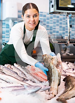 Positive saleswoman holding cod fish in fish store