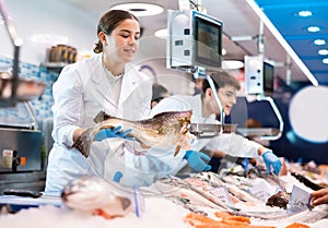 Positive saleswoman holding cod fish in fish store