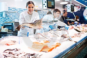 Positive saleswoman holding cod fish in fish store