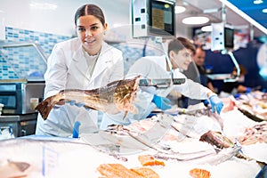 Positive saleswoman holding cod fish in fish store