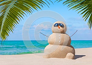 Positive sandy snowman in sunglasses at palm ocean sandy beach