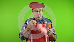 Positive senior chef shows ripe apple, talks about benefits and gives fruit.