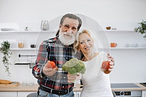 Positive senior couple man and blonde woman having fun with vegetables.