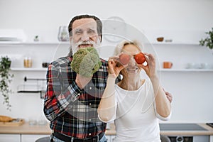 Positive senior couple man and blonde woman having fun with vegetables.