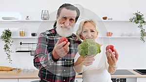 Positive senior couple man and blonde woman having fun with vegetables.
