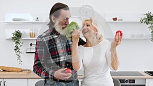 Positive senior couple man and blonde woman having fun with vegetables.