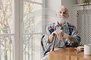 Positive senior grandfather with grey hair and beard sitting at home