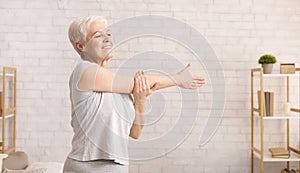 Positive senior lady warming up her hands at home