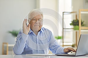 Positive senior man in shirt sitting with notebook and laptop, learning or working online