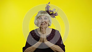 Positive senior old blond woman appealing to camera, keeping prayer gesture and asking help