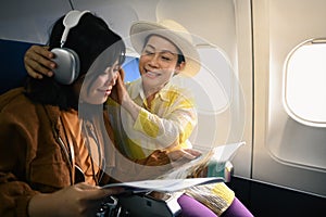 Positive senior woman and daughter listening to music during fly in airplane. Holidays and transportation concept