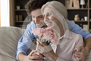 Positive senior woman getting bunch of flowers from adult son