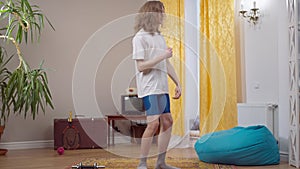 Positive skinny young man having fun training at home in 1980s 1990s. Wide shot of joyful Caucasian guy dancing to