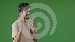 Positive smiling arab young man guy stand in green studio showing hey you gesture pretending shooting pistols making