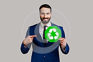 Positive smiling bearded businessman holding pointing at green recycling sign, saving environment.