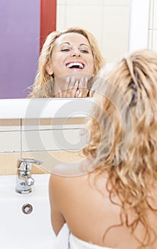 Positive and Smiling Caucasian Blond Woman Looking in Mirror and Examining Her Face