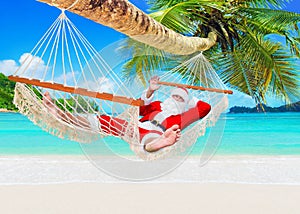 Positive smiling Christmas Santa Claus relax in hammock at island sandy ocean beach