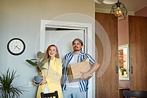 Positive smiling couple moving in new house and carrying carton boxes