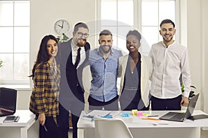 Positive smiling diverse business team hugging looking at camera in office