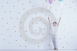 Positive smiling elderly woman with colorful balloons against white wall with gold dots