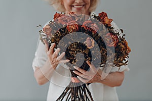 Positive smiling elderly woman hold in hands rose flowers bouquet.