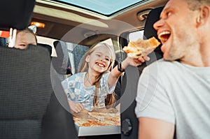 positive smiling girl putting pizza piece in father's mouth while she sitting in child car seat . Happy childhood, photo