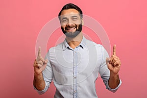 Positive and smiling Indian middle-aged man in jeans shirt points fingers up