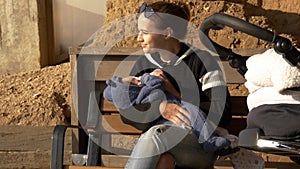 Positive and smiling mama feeding baby outdoor on a bench having rest