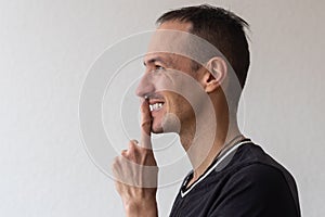 Positive smiling man with beard holding finger near lips showing shh gesture, keeping secrets preparing surprise. Indoor