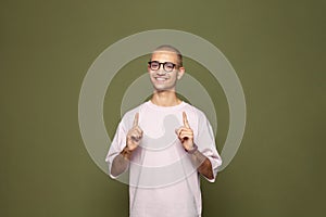 Positive smiling man wearing t-shirt posing and pointing up on green background, idea concept