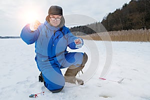 Positive smiling old man fishing on lake at cold winter day