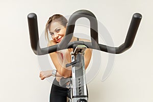 Positive smiling sporty woman peeping out from exercise bike, looking at camera, cardio workout.