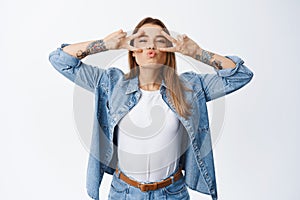 Positive smiling woman showing peace signs and pucker lips for kissing, having fun and enjoying freedom, standing upbeat