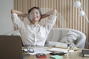 Freelancer lady sitting in front of laptop in relaxed position, eyes closed and hands behind head