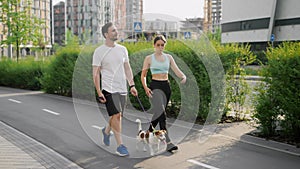 A positive sportive family spend leisure outdoors, walks and steps in unison with pet, a Jack Russell Terrier dog, on a