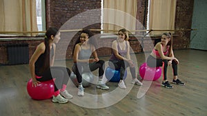 Positive sporty fit women resting on fitballs at gym