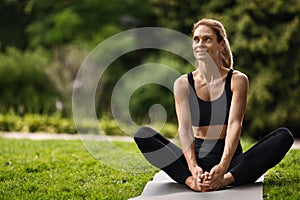 Positive sporty milennial blonde woman sitting on fitness mat