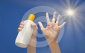 Positive symbol drawing by sunscreen on open hand. Another hand holding a bottle of sun cream. Blue sky, beams of sun background.