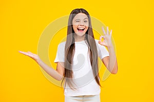 Positive teenager child points aside with cheerful expression, shows amazing at blank empty space. Advertisement and