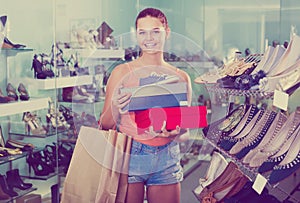 Positive teenager female holding boxes in shoes boutique