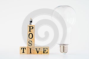 Positive thinking symbol. miniature businessman on Wooden cubes with words `positive`. light bulb. white background