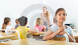Positive tween schoolgirl sitting at school desk at lesson in class