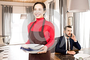 Positive waitress carrying dirty dishes away