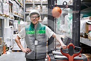 Positive warehouse worker with fork pallet truck stacker at modern warehouse
