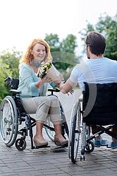 Positive wheelchaired woman getting flowers from her caring disabled husband