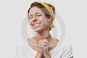 Positive wishful young woman keeps palms pressed together, hopes dreams come true, makes wish, wears yellow headband photo