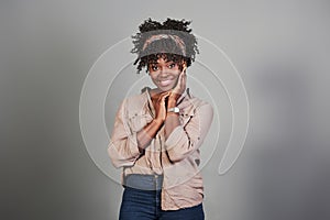 Positive woman. Cheerful african american girl keep her hands near to the face while stands at grey background