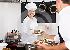 Positive woman cook giving salad to waitress