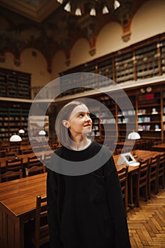 Positive woman in dark casual clothes in the library with a smile on her face and looks away